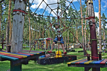 A boy walks on a tightrope on an amusement ride in a public park.
