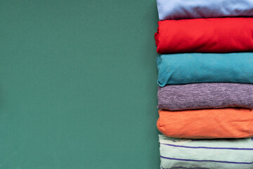 close up of rolled colorful t shirt clothes on green table background, travel and lifestyle concept