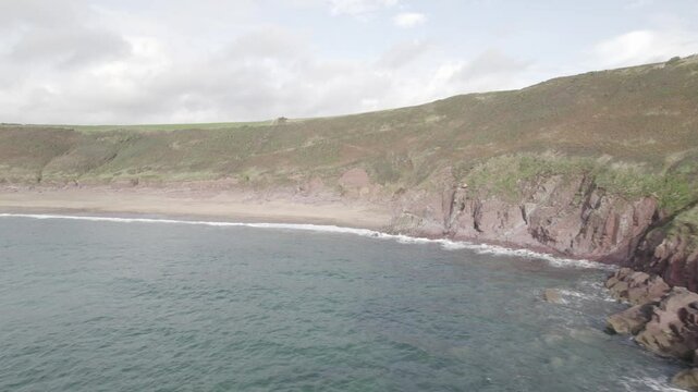Empty beach and rocky coast washed by waves. Backwards fly along seashore in bay. Manorbier, South Wales, UK