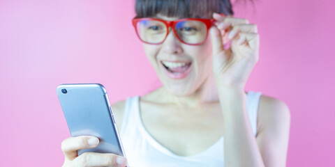 Young lady smiling wearing red eyewear hair two buns look at phone screen make wow and happy face. Portrait of astonishment, impressed. Reactions concept.