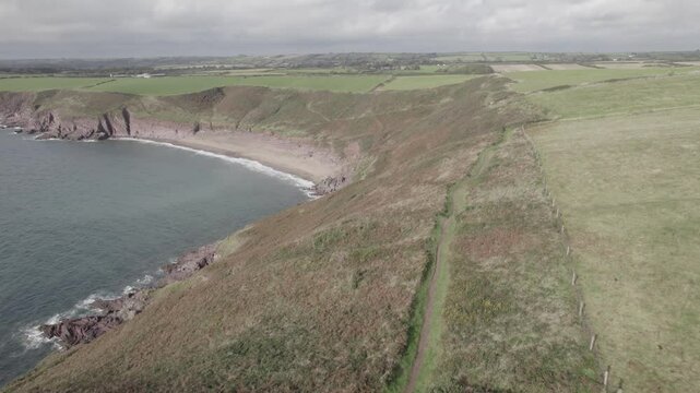 Group of hikers enjoying lookout from scenic tourist path along sea coast. Aerial view of Swanlake bay. Manorbier, South Wales, UK