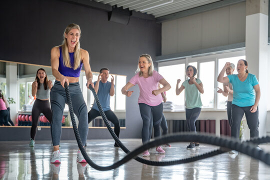 Focused woman working out with battle ropes in the gym while friends support and cheer her during a strength and endurance training session