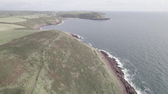  Grassy steep slope above sea coast. Aerial ascending footage of seashore and sea bay. Manorbier, South Wales, UK