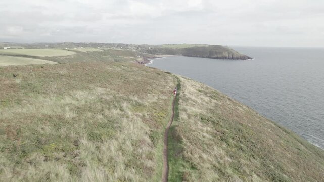  Hikers walking on scenic Pembrokeshire Coast Path high above sea surface. Aerial panoramic view of Manorbier bay. Manorbier, South Wales, UK