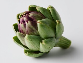 Obraz premium Fresh artichoke with its signature purple and green hues on a plain surface, showcasing its textured petals.
