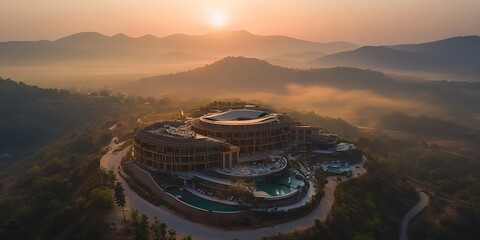 Majestic Circular Hotel Nestled in Mountains Bathed in Golden Sunset. Aerial View of Modern Architecture Enveloped by Misty Landscape. Cinematic Atmosphere for Luxury Car Advertisement Background