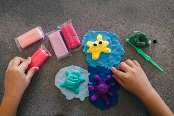 Children's hands sculpting sea animals like starfish, turtle, and octopus using bright modeling clay on a dark surface, surrounded by tools and unused clay packs