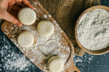 Close-up of a hand holding a raw dough round over a floured kitchen counter with baking tools in the background