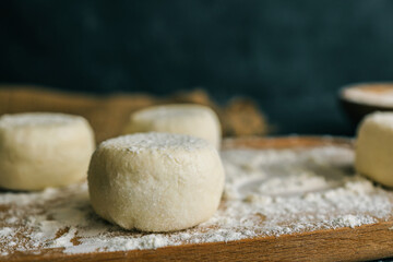 Raw dough pieces on a floured wooden board with one placed on a spoon, ready for baking on a rustic...