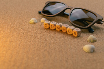 Sunglasses and seashells on cork background with wooden blocks spelling summer