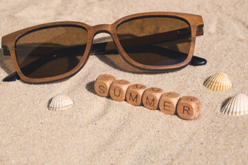 Wooden sunglasses and shells on sandy beach representing summer vibes