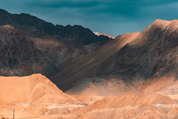 Golden hour illuminates rugged mountain peaks with sunset light casting dramatic shadows and warm tones across the rocky ridges and snowy summits