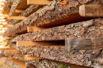 Stacked wood logs waiting to be seasoned, showcasing a natural texture with earthy tones under bright sunlight in a rural area