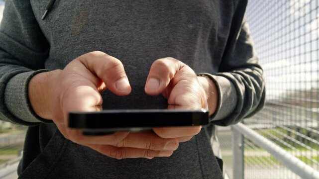 A close-up of a young man engaging with his phone on the street, framed by the warm glow of the sunset, giving a filmic touch to the shot.
