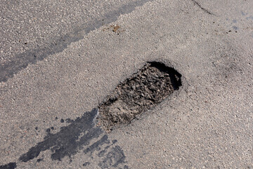 A large pothole is present on an asphalt road, creating obstacles for vehicles in a residential neighborhood during the daytime