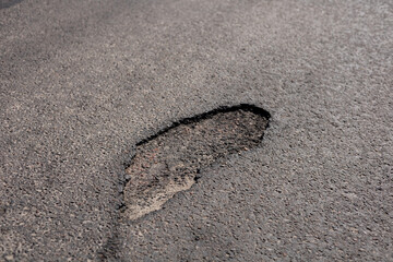 Recent heavy rain has left a substantial footprint-shaped mark in the asphalt of a city street, showing the effects of weather on infrastructure