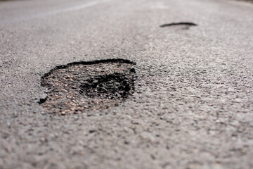 Potholes are prominently seen on the asphalt surface of a city street, indicating road maintenance...