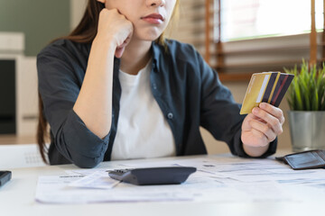 Sad Asian woman looking at many credit cards in her hand and worried about loan debt pay late.
