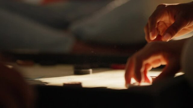 Close-up of two players engaged in a tense game of carrom, bathed in warm sunlight indoors