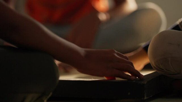 Focused hands prepare a strategic move in a cozy indoor carrom game lit by golden evening light