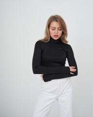 Young woman poses in stylish black top and white pants in studio setting