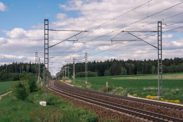 Long Modern Railway Track Running Through Meadows Under a Blue Sky with Clouds