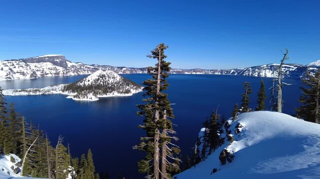snowy Landscape view of Crater Lake National Park with trees, blue sky and Wizard Island