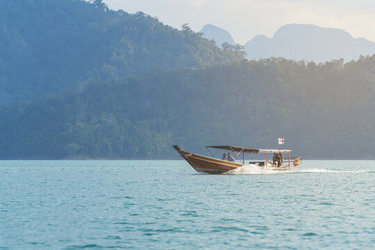 Boating and water tourism in Thailand - A longtail with tourists sailing on Cheo Lan Lake against the backdrop of high mountains
