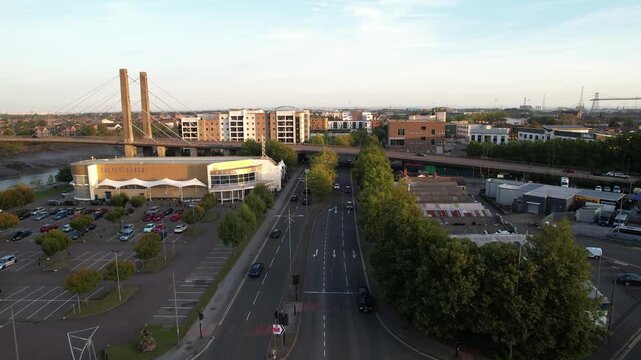 Busy multilane street and crossroads. Forwards fly above road in town and around cable stayed bridge. Newport, Wales, UK
