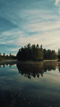 Vertical 4K scene of a remote lake with reflecting water and silhouetted trees in Temagami, Ontario