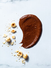 A minimalistic and appetizing image featuring a rich, glossy smear of chocolate hazelnut spread artfully arranged on a white marble surface. 