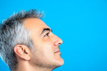 Obraz premium A fashionable man posing for a stylish portrait. Chic men's spiky hair haircut - midlife arabian man with short hair. Blue solid background. Graphic design art of style for aging men.