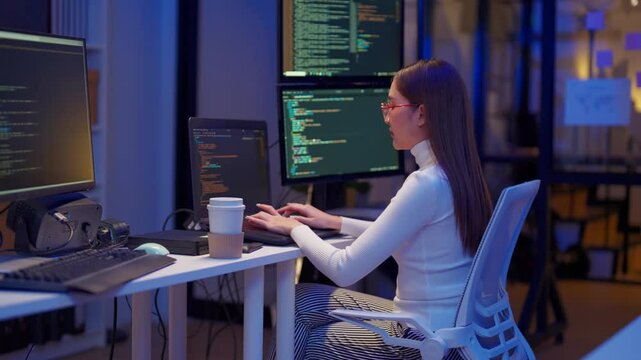 Asian programmers collaborating on software development at night, focused on writing code across multiple monitors in a tech office environment Programmers Collaborating on Software Development	