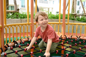 cute little boy climbing on net robes on playground in schoolyard. happy and enjoy adventure sports play alone outdoor playground.