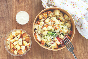 Caesar salad in a paper container, take it on the way, with sauce and croutons, on the table, snack, no people,