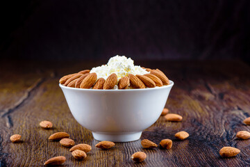 Fresh cottage cheese with almonds in a white cup on a wooden background.