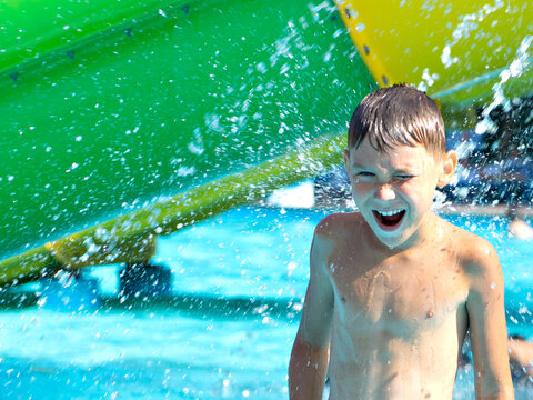 Joyful boy enjoying a splash of water at an aqua park. Bright summer day, excitement, and laughter captured in motion. Perfect image of childhood fun and outdoor recreation at a water slide