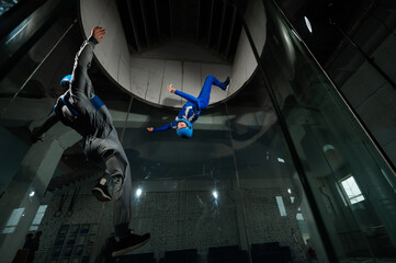 A male instructor teaches a woman how to fly in a wind tunnel. Free fall simulator.