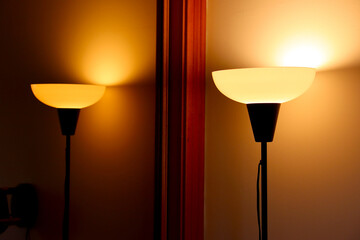 Top of a floor lamp illuminating the wall in the background, reflected in a mirror.