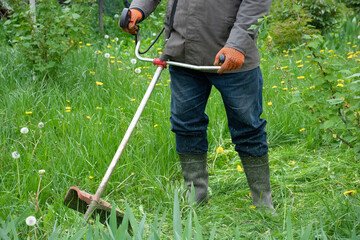 Man in the garden mowing tall grass with hand mower, garden care. High quality photo
