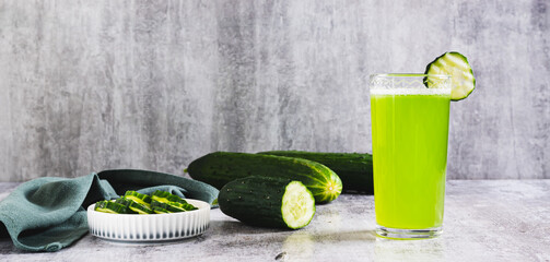 Fresh cucumber juice in a glass and cucumber pieces in a bowl on the table web banner