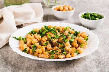 Warm salad of white fried beans and parsley on a plate on the table