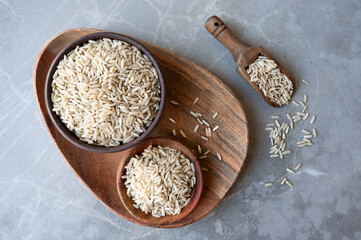 Wooden bowls of uncooked brown rice on the gray table, healthy food, whole grain.