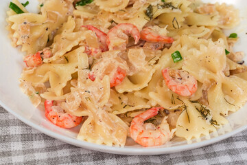 Cooked farfalle pasta with boiled shrimp tails on dish, fragment