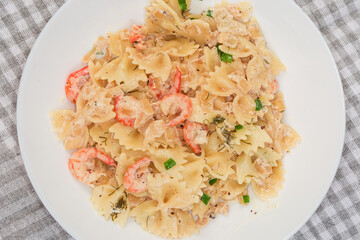 Cooked farfalle pasta with shrimp tails on dish, top view
