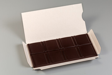 Dark chocolate bar in open paper wrapper on gray background