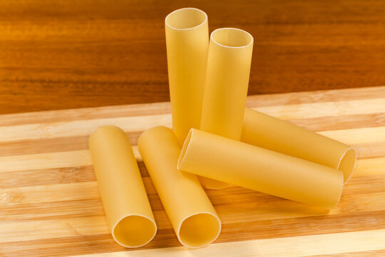 Raw large tube shaped pasta on cutting board close-up