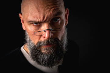 Emotional portrait of angry bearded man in glasses growling at camera, grimacing. Dramatic portrait in dim lighting, expressive face, emotional tension, dark background.