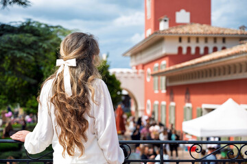 Woman posing at Chateau de Cremat with red building, and people visiting