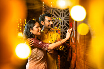 Performing Diwali ritual with thali, Indian couple marks swastik on wooden entrance door